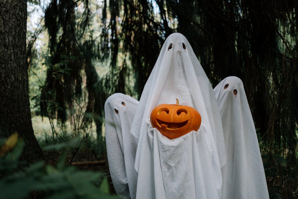 People dressed in bed sheet Halloween ghost costumes holding a pumpkin