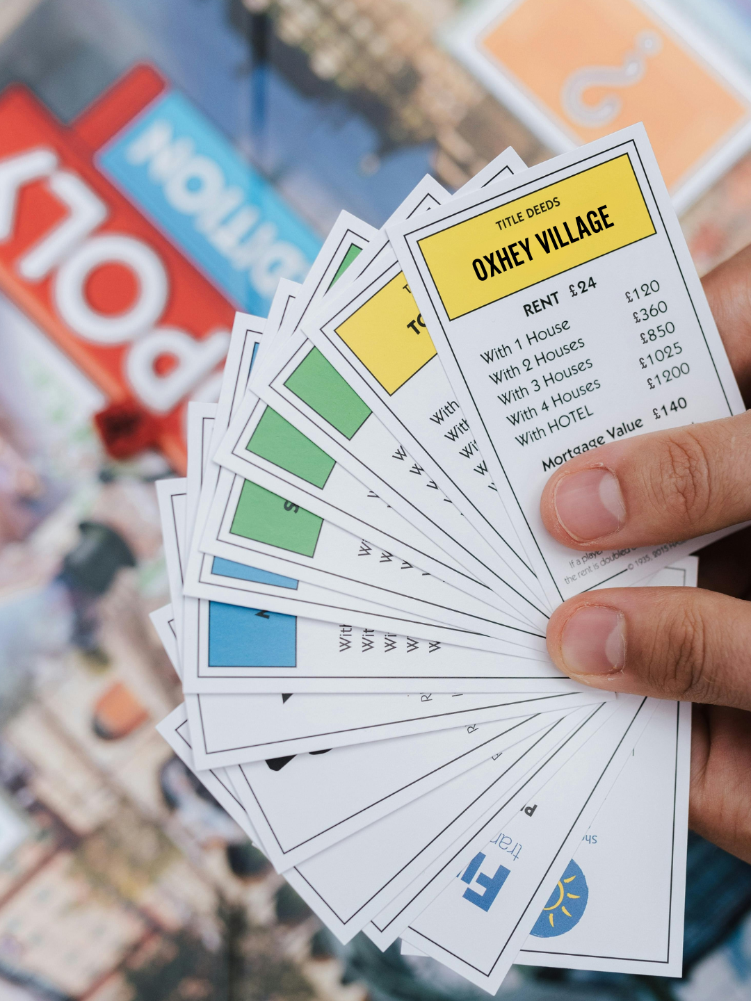 A hand holding Monopoly cards showing an Oxhey Village as part of the Watford edition